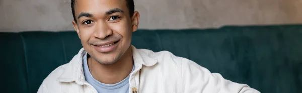 Hombre afroamericano positivo y joven mirando a la cámara en la cafetería, pancarta - foto de stock