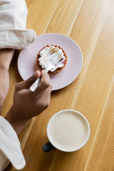 Vue de dessus de l'homme afro-américain tenant fourchette près de tarte et tasse de cappuccino — Photo de stock