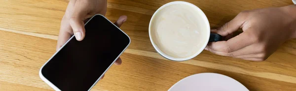 Vista superior do homem americano africano segurando smartphone e xícara de cappuccino, banner — Fotografia de Stock