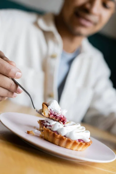 Vista cortada de homem americano africano desfocado comendo bolo saboroso no café — Fotografia de Stock