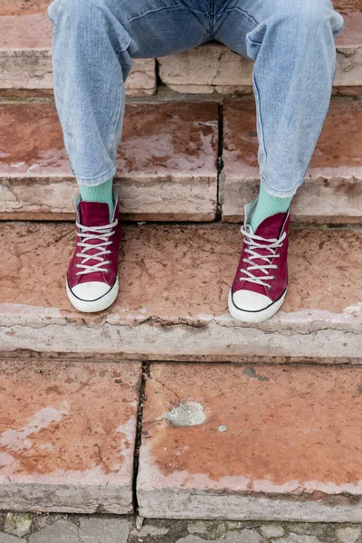 Cropped view of man in jeans and sneakers sitting on stairs — Stock Photo
