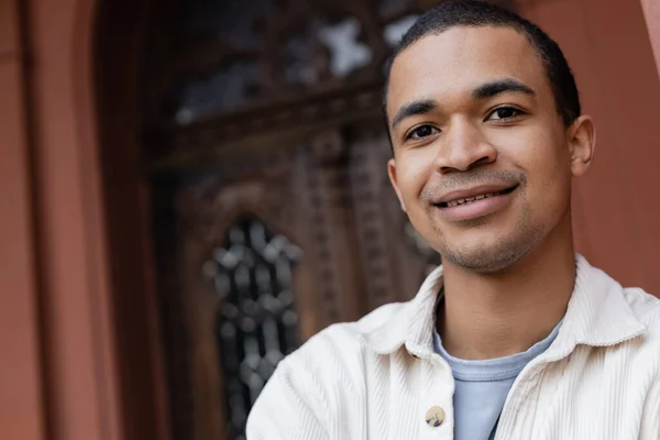 Glücklicher afrikanisch-amerikanischer Mann in Hemdjacke lächelt in der Nähe eines Gebäudes in Europa — Stockfoto