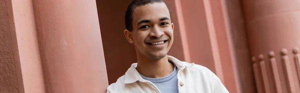 Cheerful african american man in shirt jacket standing near building, banner — Stock Photo