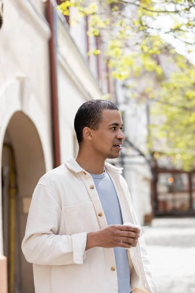 Africano americano hombre en camisa chaqueta celebración takeaway bebida en urbano ciudad - foto de stock