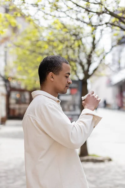 Side view of young african american man in shirt jacket holding takeaway drink in urban city — Stock Photo