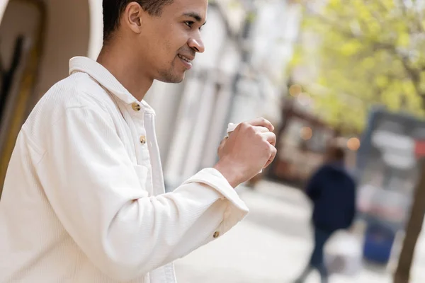 Side view of happy african american man in shirt jacket holding takeaway drink outside — Stock Photo