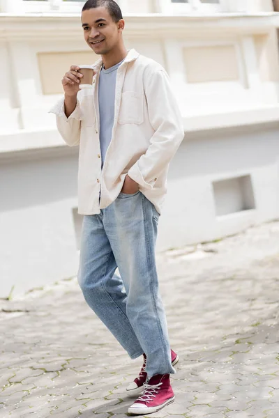 Comprimento total de homem americano africano feliz em camisa jaqueta segurando café para ir e caminhar na cidade urbana — Fotografia de Stock