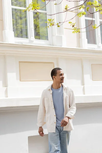 Junger und zufriedener afrikanisch-amerikanischer Mann in Hemdjacke spaziert durch urbane Stadt — Stockfoto
