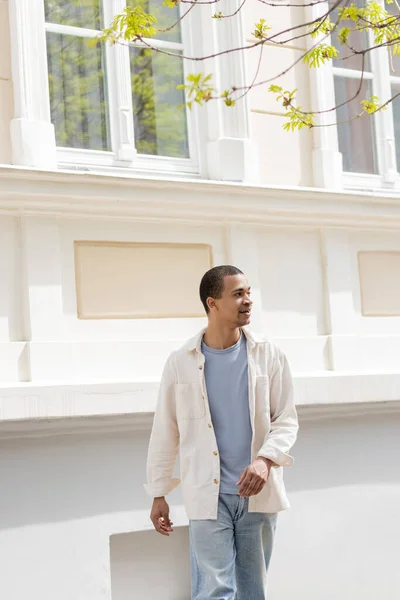 Young and pleased african american man in shirt jacket walking in urban city — Stock Photo