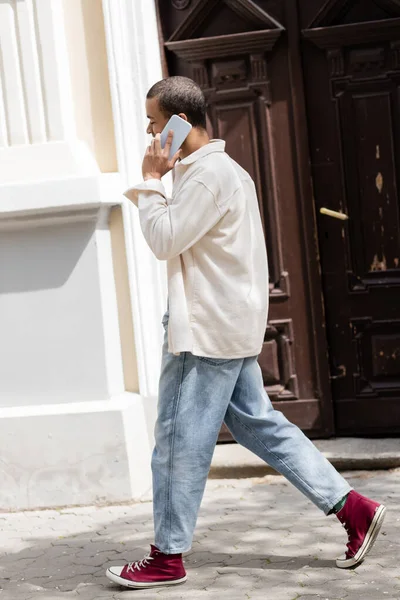 Full length of african american man in shirt jacket talking on mobile phone on street in urban city — Stock Photo