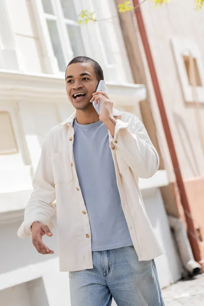 Emotional african american man in shirt jacket talking on mobile phone on street in urban city — Stock Photo