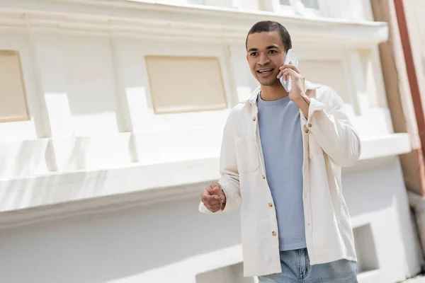 Joven afroamericano hombre en camisa chaqueta hablando por teléfono móvil en ciudad urbana - foto de stock