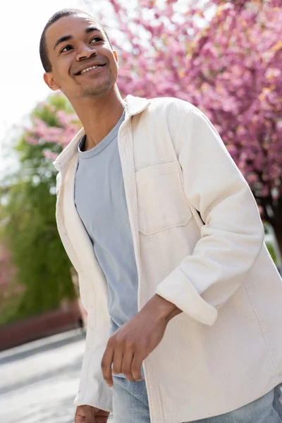Uomo afroamericano in camicia giacca camminare vicino albero di ciliegio rosa — Foto stock
