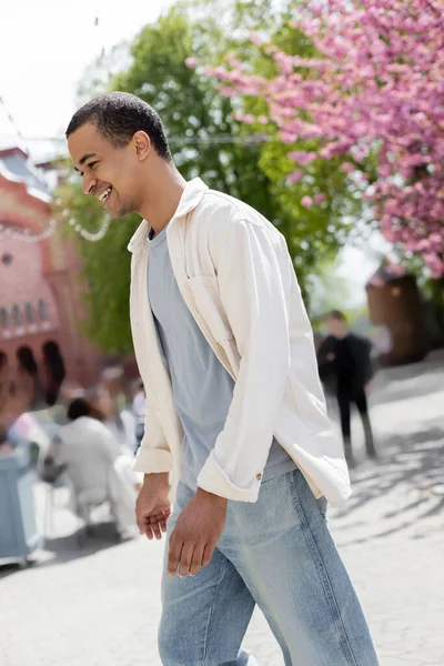 Uomo afroamericano in camicia giacca camminare vicino albero di ciliegio rosa — Foto stock