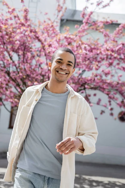 African american man in shirt jacket walking near pink cherry tree — Stock Photo