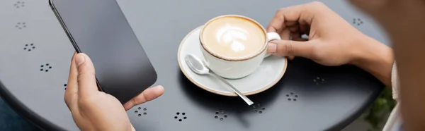 Partial view of african american man texting on smartphone near cappuccino on table, banner — Stock Photo