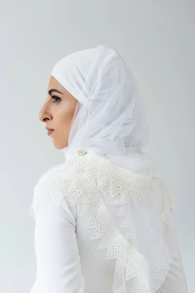 Side view of muslim bride in hijab and white dress isolated on grey — Stock Photo