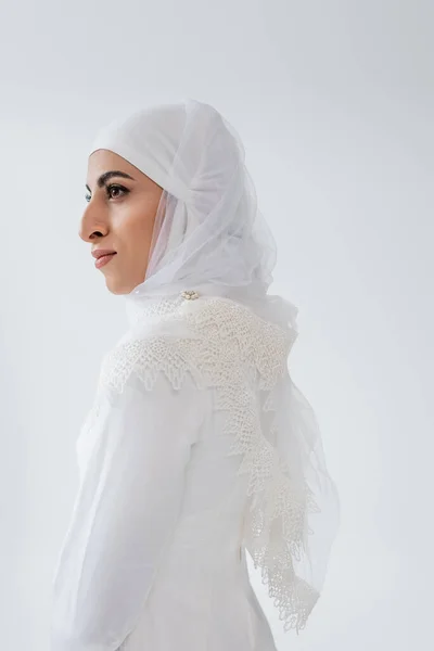 Молодая мусульманка в хиджабе и свадебном платье, смотрящая в сторону изолированной на сером — стоковое фото