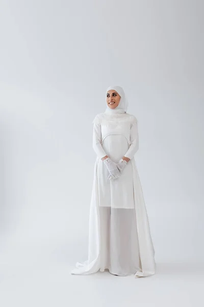 Volle Länge der glücklichen muslimischen Frau im Hijab und Hochzeitskleid auf grau — Stockfoto