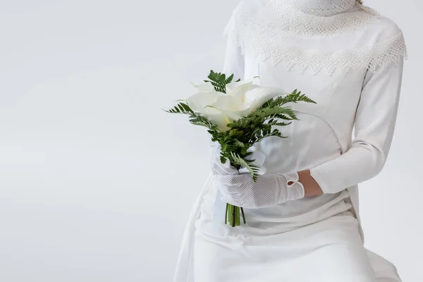 Vista cortada da noiva em luvas e vestido de noiva segurando flores de lírio calla isolado em cinza — Fotografia de Stock