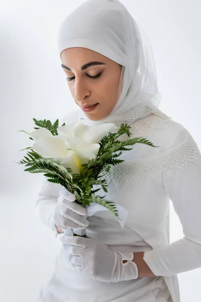 Mariée musulmane en gants et robe de mariée sentant calla fleurs de lis isolé sur gris — Photo de stock