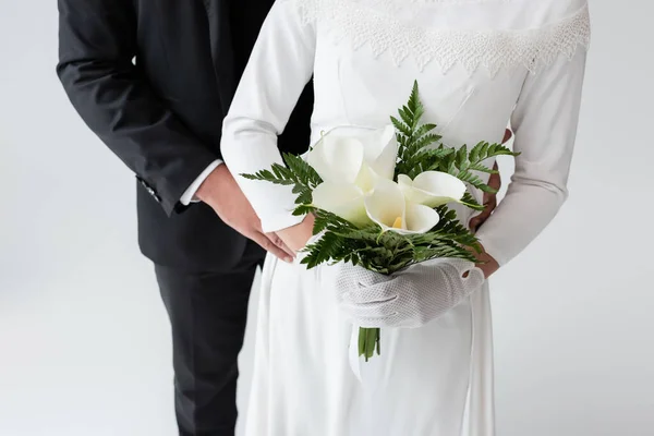 Cropped view of groom hugging bride in wedding dress with bouquet isolated on grey — Stock Photo