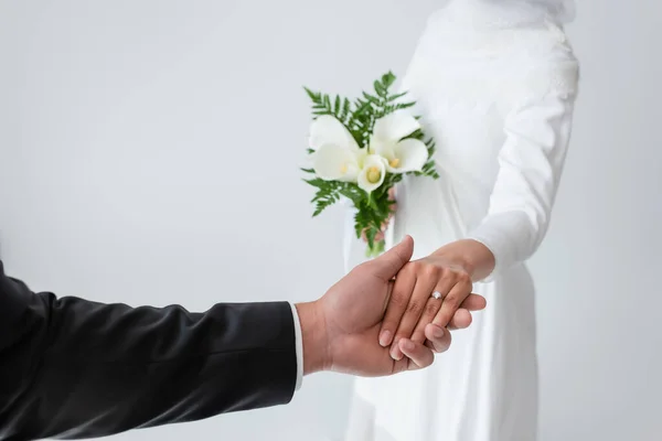 Cropped view of bride with bouquet holding hands with blurred groom isolated on grey — Stock Photo