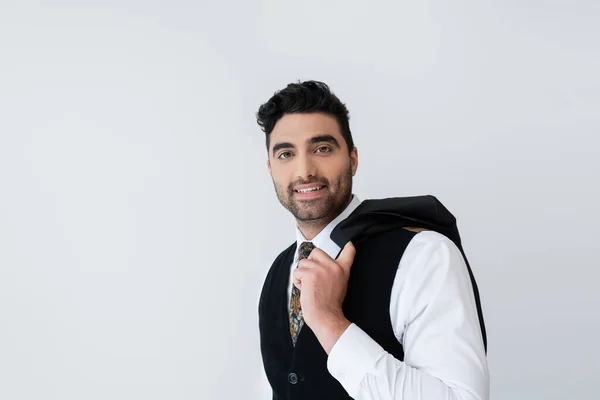 Happy muslim man in vest holding blazer isolated on grey — Stock Photo