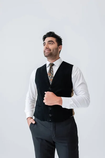 Hombre musulmán feliz en chaleco de pie con la mano en el bolsillo y sonriendo aislado en gris — Stock Photo