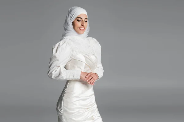 Cheerful muslim bride in wedding dress and hijab smiling on dark grey — Stock Photo