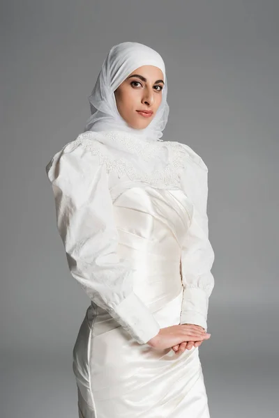 Giovane sposa musulmana in abito da sposa e hijab guardando la fotocamera su grigio scuro — Foto stock