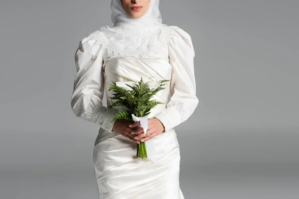 Vista cortada de noiva muçulmana em vestido branco e hijab segurando buquê de casamento em cinza escuro — Fotografia de Stock