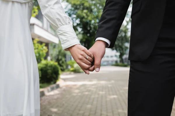 Cropped view of bride in wedding ring holding hands with groom outdoors — Stock Photo