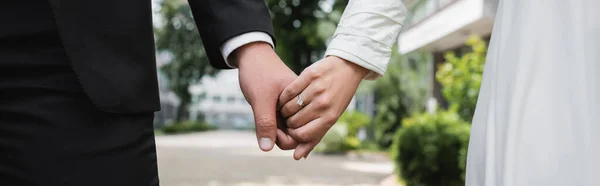 Vista ritagliata della sposa nella fede nuziale che si tiene per mano con lo sposo all'aperto, banner — Foto stock