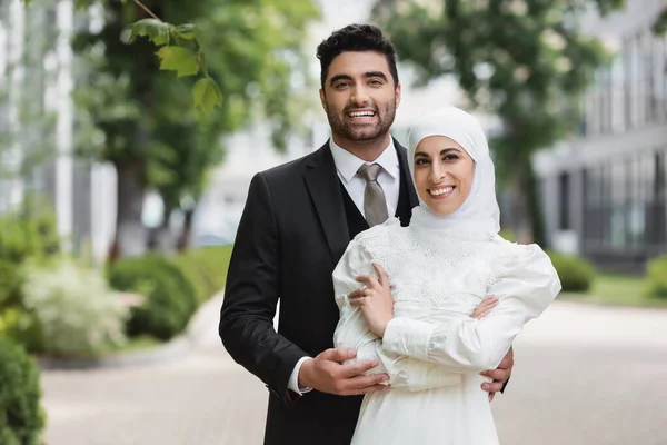Счастливый жених обнимает мусульманскую невесту в хиджабе с обручальным кольцом — стоковое фото