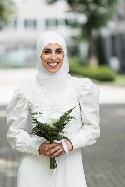 Feliz novia musulmana con anillo de diamante en el dedo celebración de ramo de boda - foto de stock