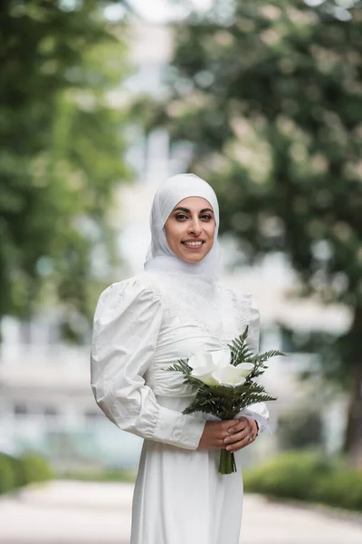 Улыбающаяся мусульманская невеста с бриллиантовым кольцом на пальце, держащая свадебный букет — стоковое фото
