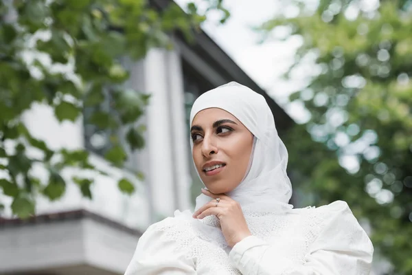Vista de ángulo bajo de la novia musulmana en hijab con anillo de diamantes en el dedo mirando hacia otro lado - foto de stock