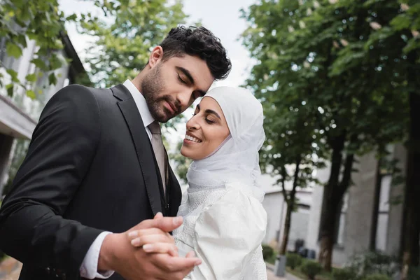 Alegre musulmán recién casados con los ojos cerrados cogidos de la mano - foto de stock