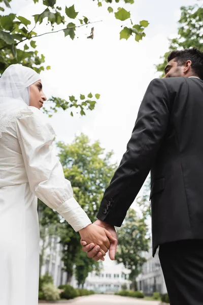 Low angle view of groom and muslim bride holding hands — Stock Photo