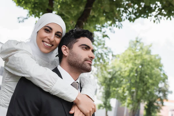 Zufriedene Braut im Hijab umarmt muslimischen Bräutigam im Anzug — Stockfoto