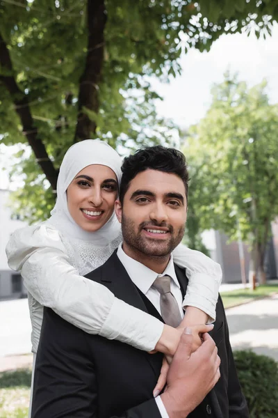 Zufriedene Braut im Hijab umarmt fröhlichen muslimischen Bräutigam im Anzug — Stockfoto