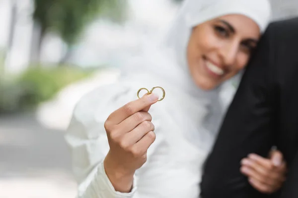 Feliz y borrosa novia musulmana celebración de la boda anillos de oro en la mano - foto de stock