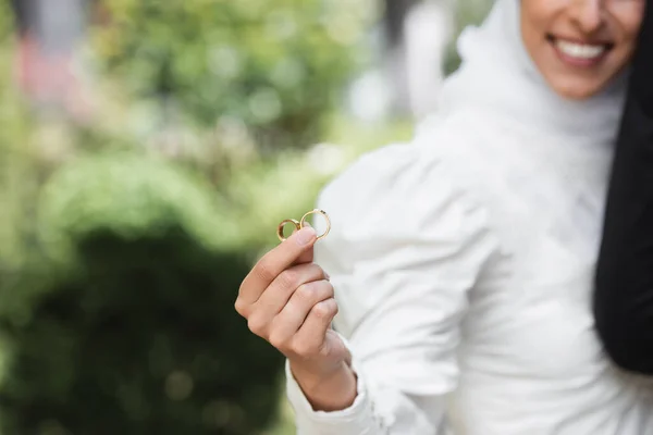 Vista cortada de noiva muçulmana feliz e borrada segurando anéis de ouro do casamento na mão — Fotografia de Stock