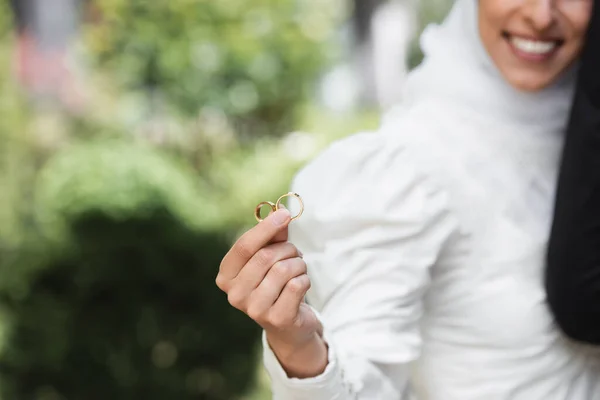 Vista recortada de feliz y borrosa novia musulmana celebración de anillos de oro de la boda en la mano - foto de stock