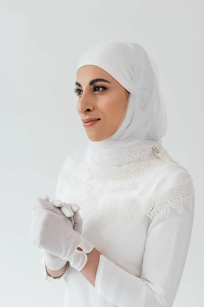 Portrait de mariée musulmane souriante en hijab blanc et robe de mariée regardant loin isolé sur gris — Photo de stock