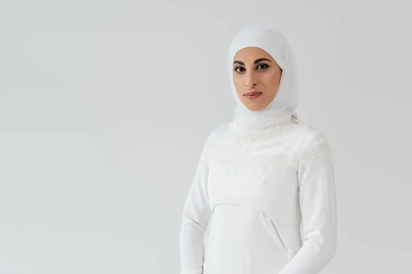 Porträt einer muslimischen Braut in weißem Hijab und Brautkleid, die isoliert auf grau in die Kamera blickt — Stockfoto