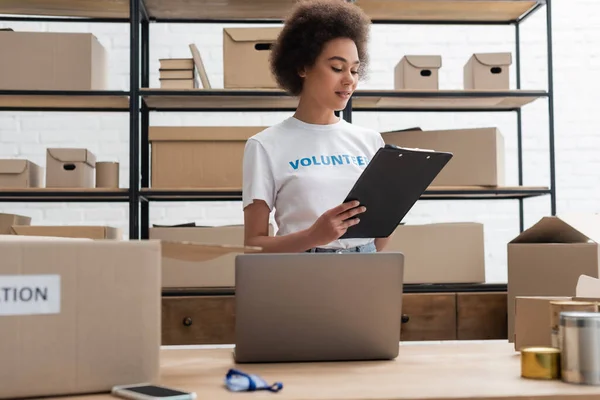 African american volunteer looking at clipboard while working in donation center — Fotografia de Stock