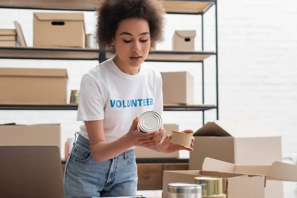 Young african american woman sorting canned foodstuff in volunteer center — Fotografia de Stock