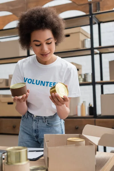 African american volunteer holding canned food in donation storehouse — Stockfoto